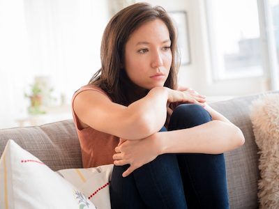 A young woman sitting on her couch looking sad